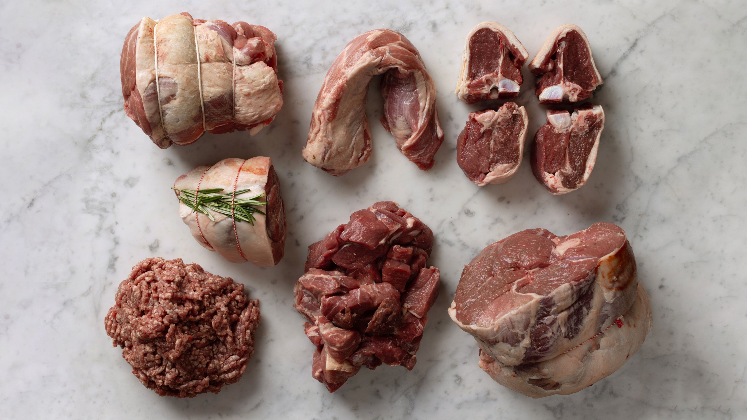 A top-down spread of dry-aged lamb cuts on butcher paper, shot from above on the Salter and King counter in Aldeburgh